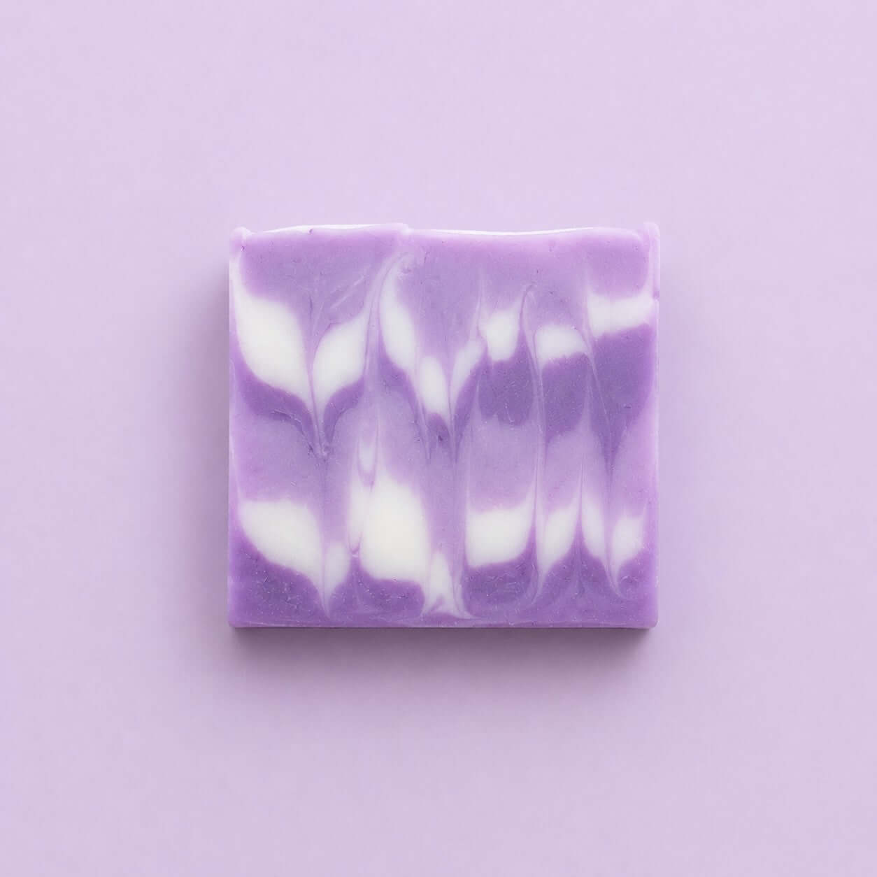Bio Seife 'Lavendel' mit lila-weißen marmorierten Mustern auf einem pinken Hintergrund.