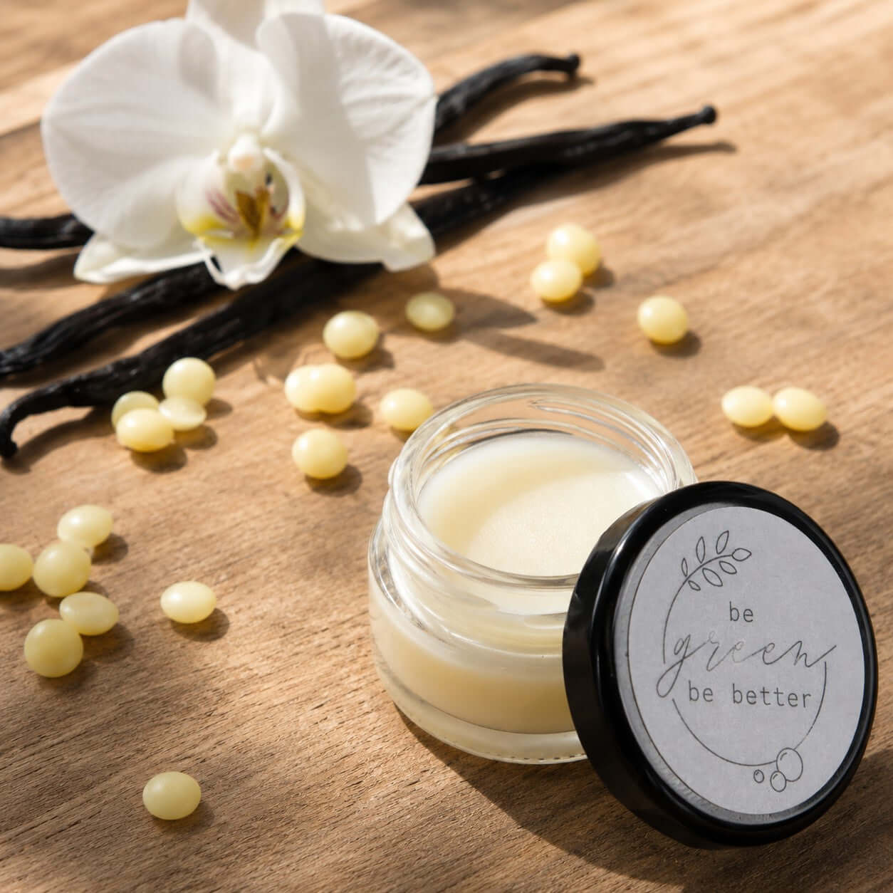 Veganer Bio Lippenbalsam mit Vanillearoma in Glasbehälter mit Zutaten als Deko